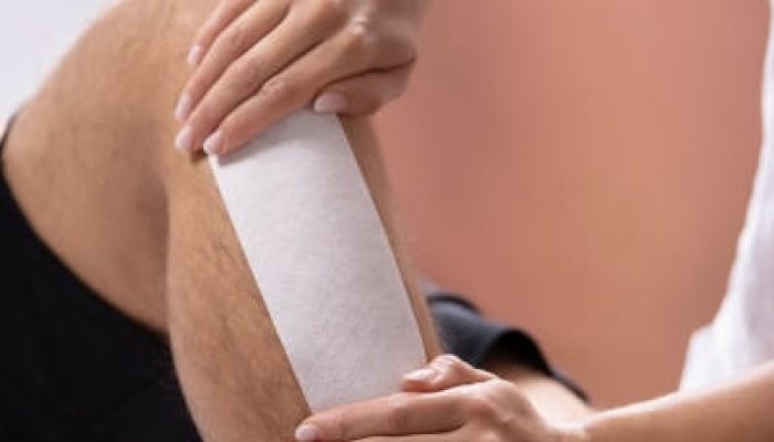 Close-up Of Therapist Hand Waxing Man's Leg With Wax Strip